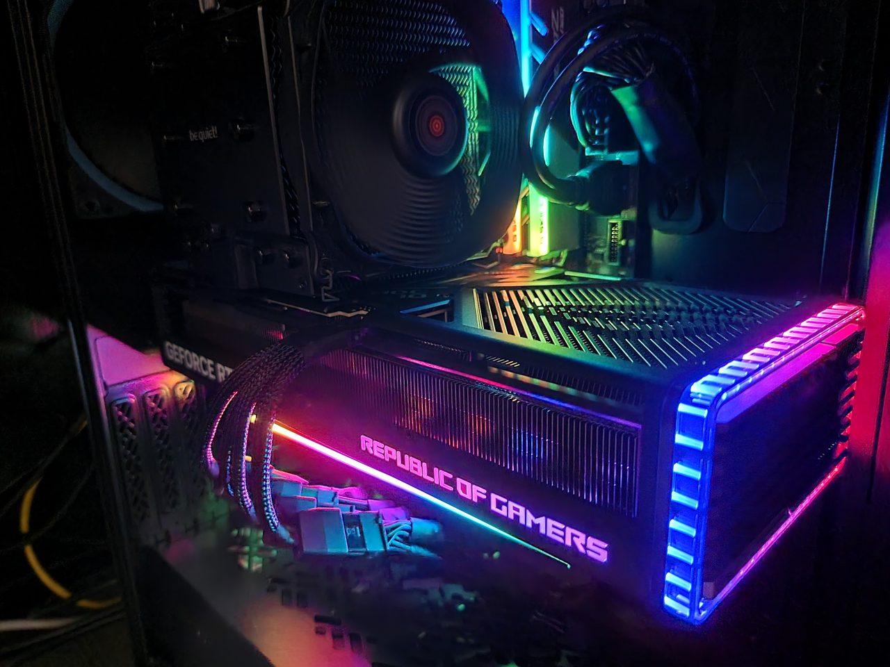 An ASUS ROG Strix NVIDIA GeForce RTX 4090 graphics card installed and running inside an open custom gaming PC build, its fans illuminated.