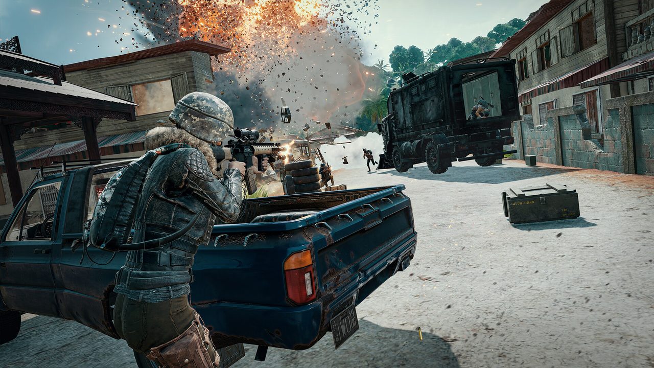 A player firing a scoped rifle from the bed of a pickup truck at a tropical village as a vehicle explodes and armed figures scatter near a black armored truck.